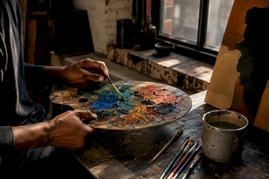 Hands mixing jewel and earth tone paints on palette