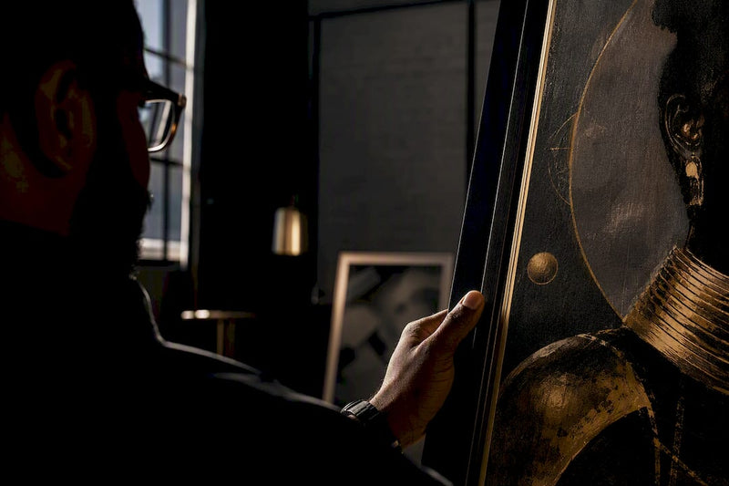 Black collector studying framed artwork at home