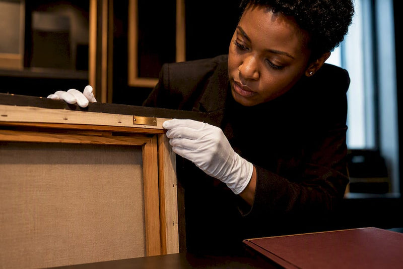 Curator inspecting provenance details on framed artwork