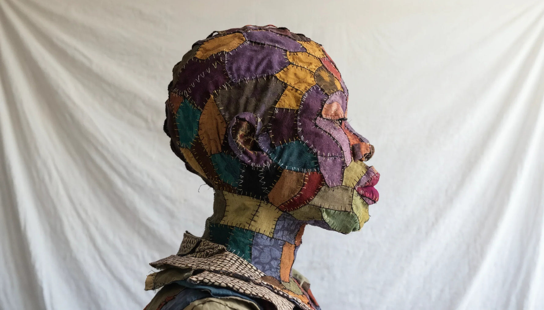 Life size portrait of a person made entirely from layered patterned cotton fabric, with skin pieced in purples, ochres and teals.