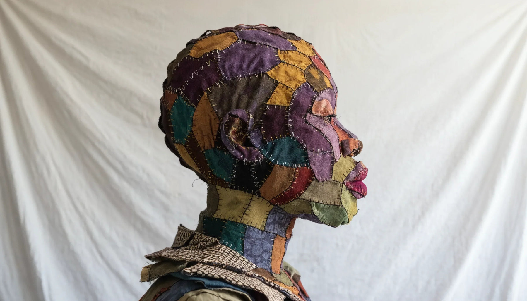 Life size portrait of a person made entirely from layered patterned cotton fabric, with skin pieced in purples, ochres and teals.