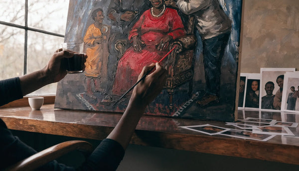 An artist's hands painting a commissioned family-story canvas in a warm studio with reference photos, no face.