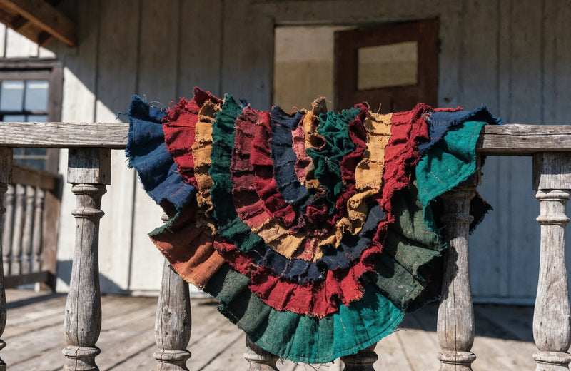 A colorful Gullah rag quilt made of red, indigo, ochre and green cloth strips draped over a weathered porch rail
