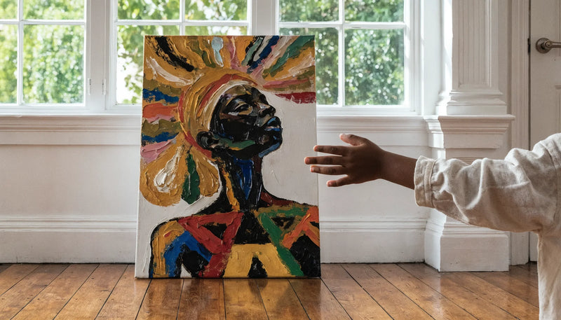 A child's small hand reaching toward a colorful joyful original Black-art canvas in a bright room, no face.