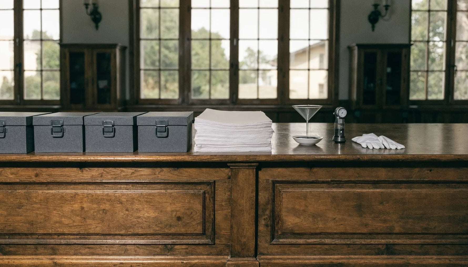 A conservation lab bench with plain archival boxes, buffered tissue, a pH testing setup, a light meter and folded cotton gloves.