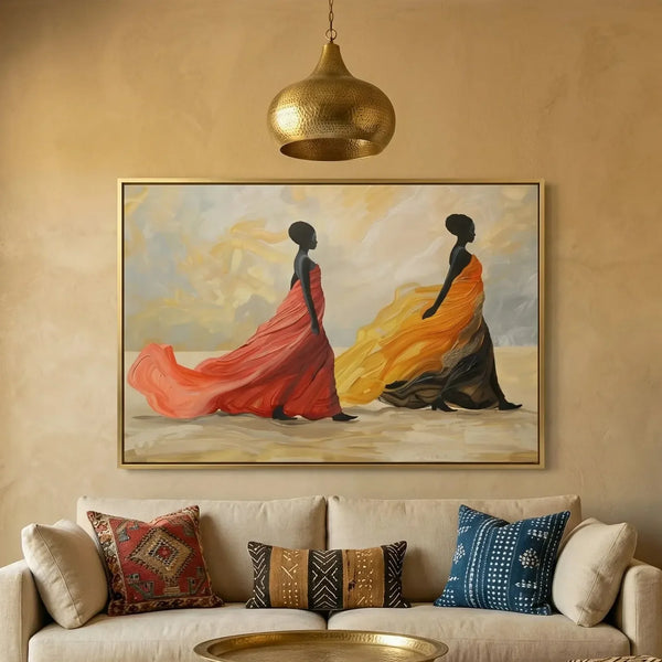 African wall art of two women in flowing red and gold gowns, gold framed canvas above a cream sofa with kilim pillows