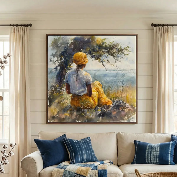 Gullah Geechee wall art above a cream sofa with indigo pillows, woman in a yellow headwrap resting under a coastal tree