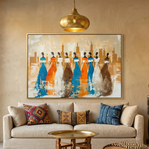 Ancestors African village wall art canvas featuring nine tribal women in blue and orange gowns, above a cream sofa in a Moroccan plaster living room