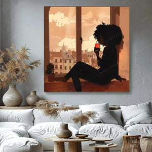 Melanin art canvas of a Black woman sipping red wine in a window at dusk, above a white sofa with pampas grass