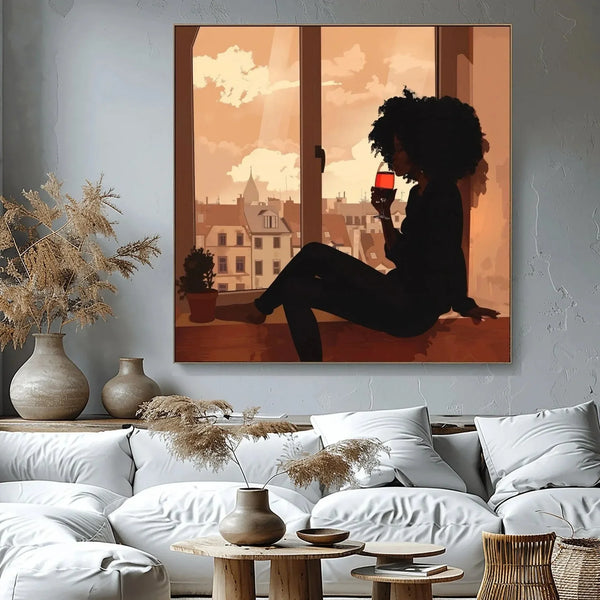 Melanin art canvas of a Black woman sipping red wine in a window at dusk, above a white sofa with pampas grass