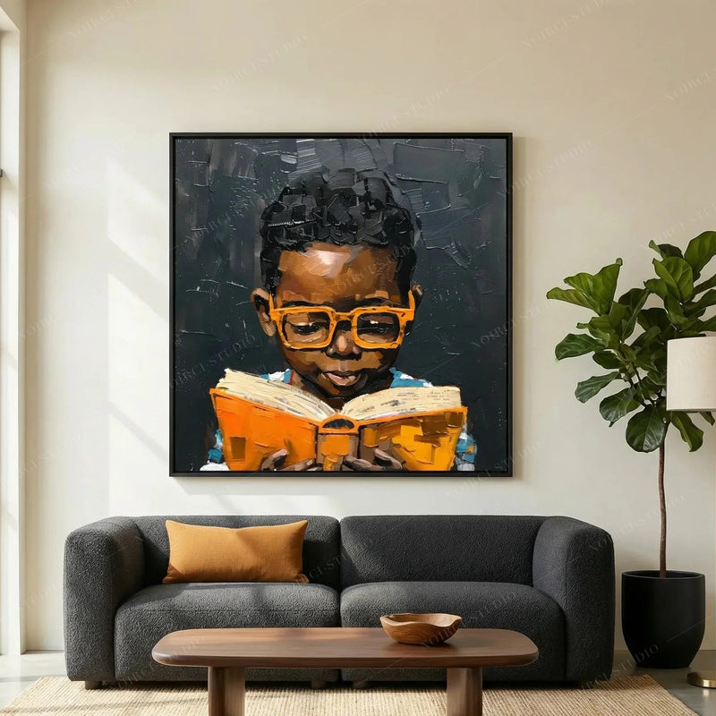 Black Boy Joy Reading wall art above a charcoal sofa, showing an oil painting of a young Black boy in orange glasses reading a book