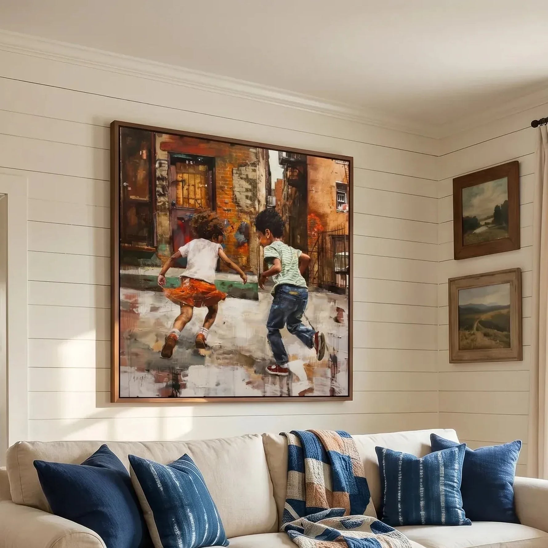Black art for living room walls, kids running scene in a walnut frame above a cream sofa with indigo pillows