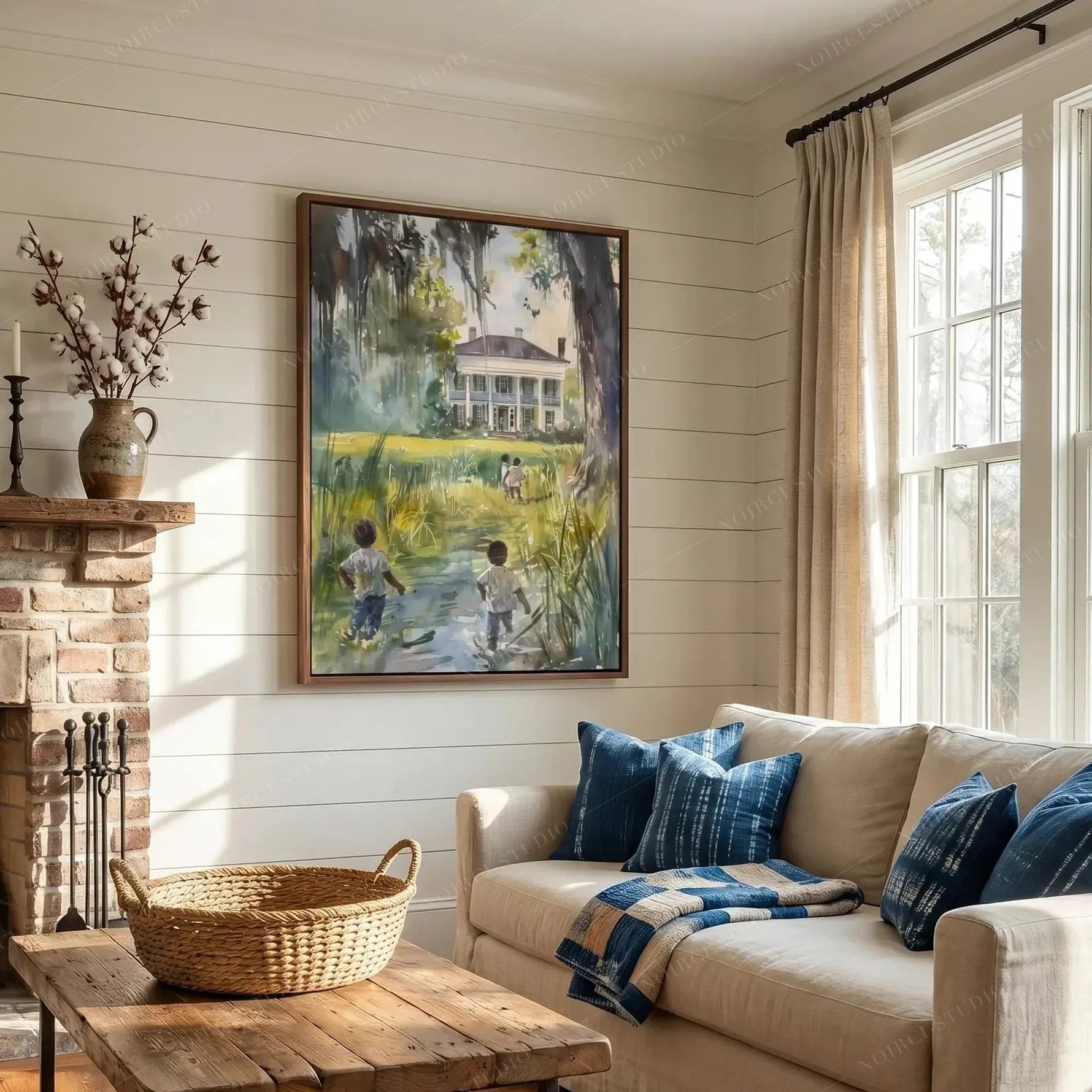 Framed lowcountry watercolor above a cream sofa with indigo pillows, shiplap living room with a brick fireplace