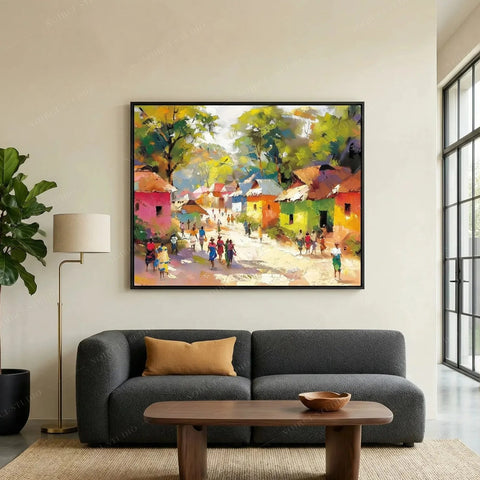African landscape painting in a black frame above a dark gray sofa, colorful village scene with figures on a sunlit path