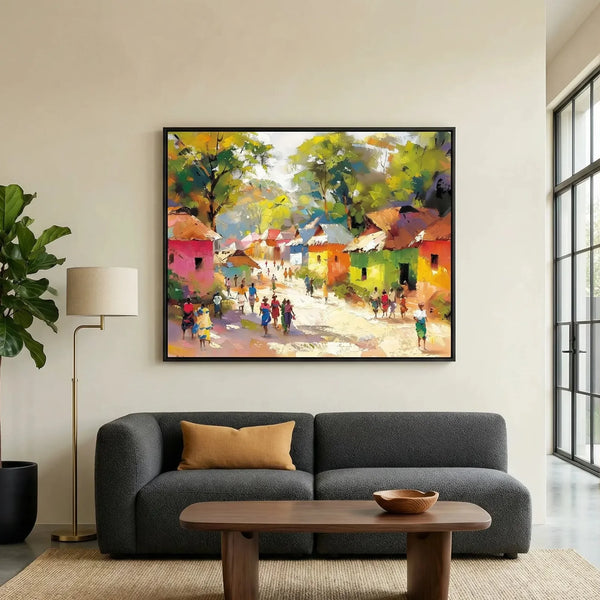 African landscape painting in a black frame above a dark gray sofa, colorful village scene with figures on a sunlit path